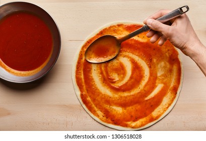 Chef Hand Spreading Tomato Paste On Raw Pizza Base, Top View