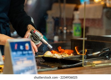 Chef hand using torch gas burner cooking grilled seafood tuna meat bbq on sticks serving to customer at street market in Tokyo city, Japan. Japanese street food and holiday travel vacation concept.