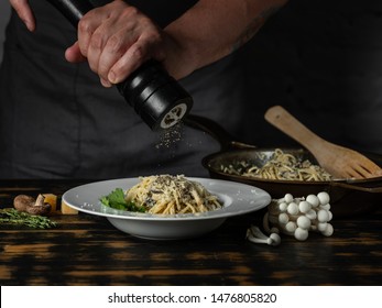 Chef hands adding paper in dish and cooking Italian pasta carbonara with cheese parmesan and white creamy sauce on wooden table background.