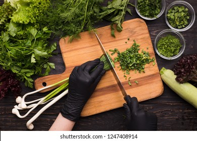 Chef Hands In Black Gloves Cutting Spring Onion On Wooden Board, Kitchen Table With Fresh Organic Vegetables, Top View