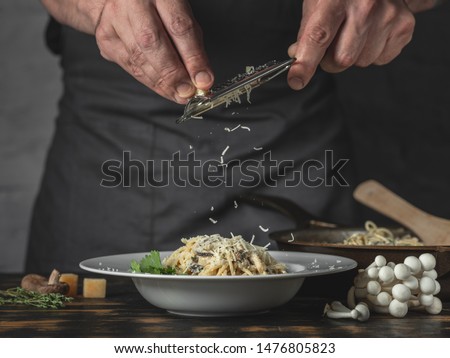 Chef hands cooking Italian pasta and adding cheese parmesan in dish on wooden table background.