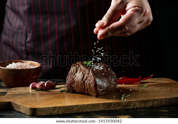 Chef\
hands cooking meat steak and adding salt and pepper on black copy\
space background for menu restaurant or recipe\
text.