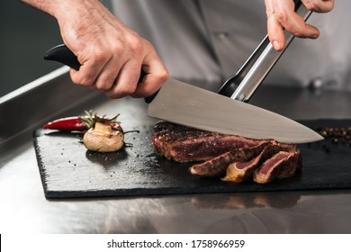 Chef Hands Cut Grill Steak At Kitchen Restaurant. Closeup Chef Hands Cut Meat. Professional Cutting Grill Meat At Chopping Board.