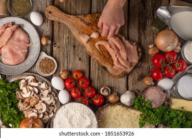 Chef hands cuts with knife chicken fillet on wooden chopped board with variety of ingredients background. Concept of cooking process. Backstage of preparing tasty meal. View from above. Flat lay. - Powered by Shutterstock