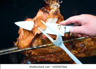 Chef Hands cutting whole grilled pork for steaks with knife. Pig grilled traditional coal and fire. The little pig is roasted whole on an open fire. Pig on the spit