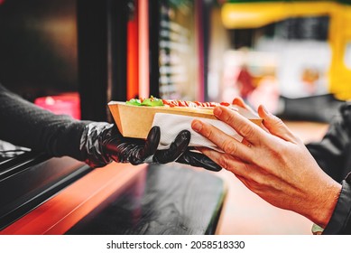 chef hands gives a hot dog to man from food truck on street. street food, fast food. - Powered by Shutterstock