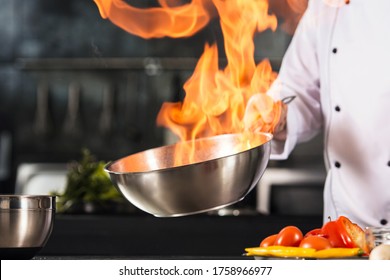 Chef hands hold wok with fire. Closeup chef hands prepare food with fire. Cook burn food at professional kitchen. - Shutterstock ID 1758966977