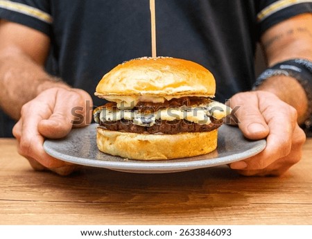 Chef hands holding a hamburger with bread, meat, gorgonzola cheese onion and sausage. Delicious fast food burger prepared on a restaurant kitchen.Professional chef holding a burger ready to eat.