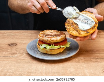 Chef hands preparing a hamburger with bread, salad, meat, cheese and sausage. Delicious fast food burger prepared on a restaurant kitchen. Professional chef is preparing burger. Burger making.