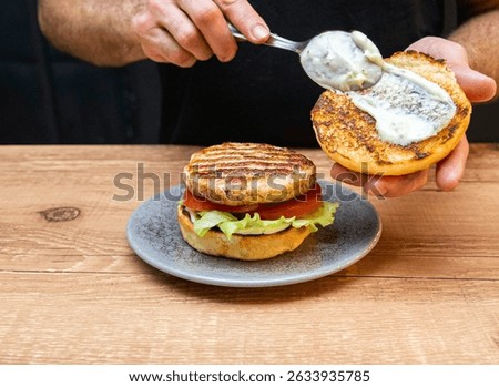 Chef hands preparing a hamburger with bread, salad, meat, cheese and sausage. Delicious fast food burger prepared on a restaurant kitchen. Professional chef is preparing burger. Burger making.