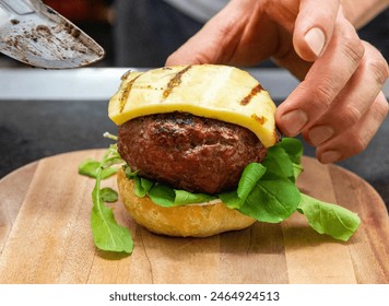 Chef hands preparing a hamburger with salad, meat and cheese. Delicious fast food burger prepared on a restaurant kitchen. Professional chef is preparing burger. Burger making. - Powered by Shutterstock