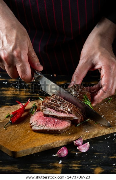 Chef hands slicing beef\
steak with knife on wood cutting desk. Top view food preparation\
process concept.