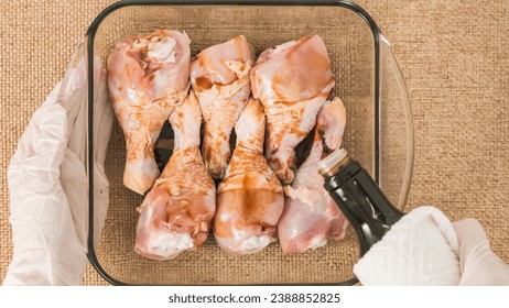 Chef hands wearing gloves pouring soy sauce  into a glass baking dish with chicken drumsticks in it. Marinated chicken meat recipe - Powered by Shutterstock