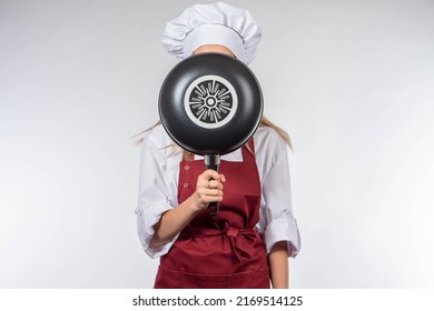 Chef Hides His Face. Frying Pan In Front Face Of Girl Cook. Woman Restaurant Employee. Lady With Frying Pan In Front Her Head. Anonymous Cook On Light Background. Concept Cook Recommends Frying Pan