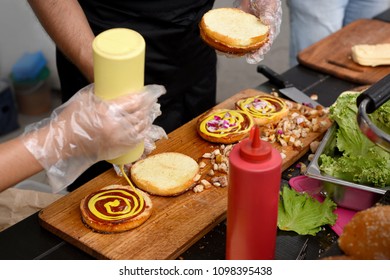 chef and his assistant adding mustard and ketchup to burgers grilled for outdoors barbecue - Powered by Shutterstock