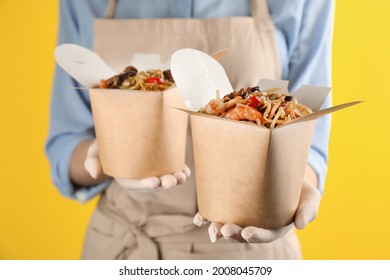 Chef holding boxes of wok noodles with seafood on yellow background, closeup