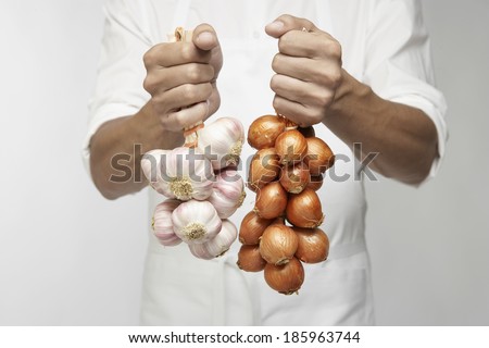 Chef holding bunch of garlic and shallot onions (mid section)