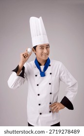 Chef holds an egg and smiles while wearing a hat and white uniform in a simple background