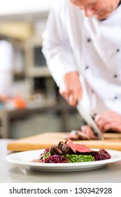 Chef In Hotel Or Restaurant Kitchen Cooking, He Is Cutting Meat Or Steak For A Dish On Plate