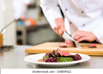 Chef In Hotel Or Restaurant Kitchen Cooking, Only Hands, He Is Cutting Meat Or Steak For A Dish On Plate