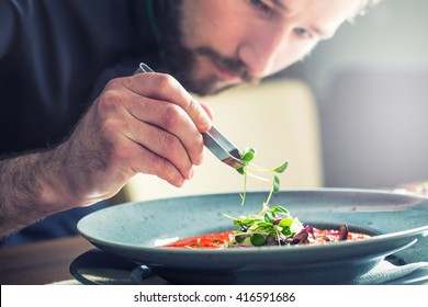 Chef in hotel or restaurant kitchen cooking only hands. He is working on the micro herb and preparing tomato soup. - Shutterstock ID 416591686
