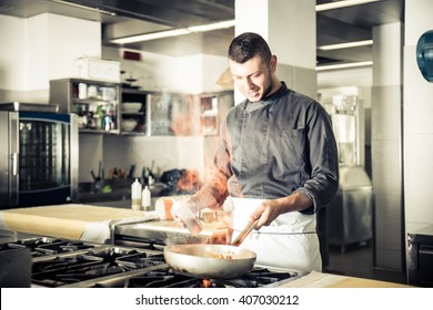 Chef in hotel or restaurant kitchen working and cooking - Chef in restaurant kitchen at stove with pan, doing flambe on food - Powered by Shutterstock