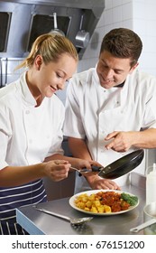 Chef Instructing Trainee In Restaurant Kitchen