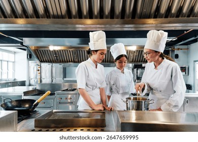 Chef instructing two culinary students in white uniforms and tall hats on how to cook in a commercial kitchen, standing near a pot on the stove during a hands-on professional cooking class.