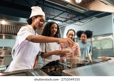 Chef instructor demonstrating cooking technique to teenage culinary students in professional kitchen classroom. Concept of hospitality education and chef mentorship.