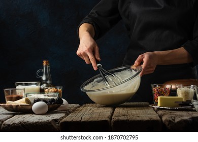 The chef kneads the dough in glass bowl. Backstage of cooking waffle on rustic wooden table with ingredients on dark blue background. Frozen motion. Traditional recipe. Cooking process. - Powered by Shutterstock