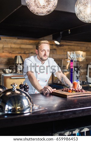 Chef leaning on the counter with a dish in a commercial kitchen