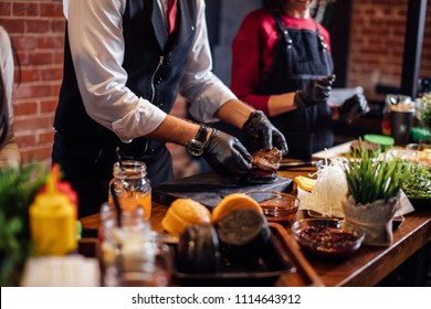 Chef Making Beef Burgers Indoor At Restaurant Kitchen, Participating In Food Festival Event.