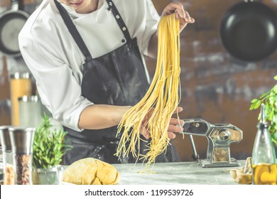 Chef making spaghetti noodles with pasta machine on kitchen table with some ingredients around. 