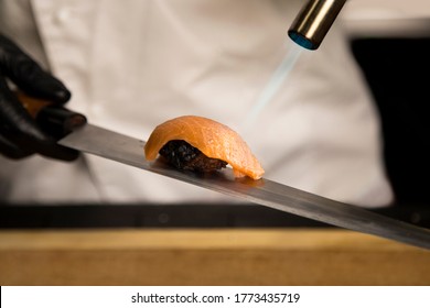 Chef Making Traditional Sushi Nigiri With Black Rice. Close Up Of Preparing Asian Salmon Tataki. Sake Nigiri Cooking Process In Restaurant. Roasting Salmon On Japanese Knife With Fire. Burning Food