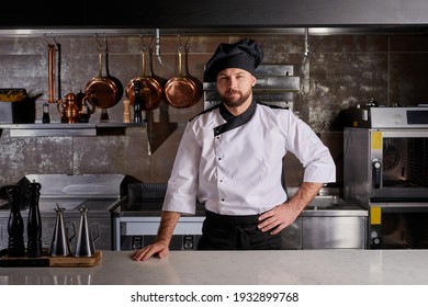 Chef man at kitchen restaurant posing at camera standing by table in uniform. Portrait of confident male chef at work. Professional Cook look at camera seriously - Powered by Shutterstock