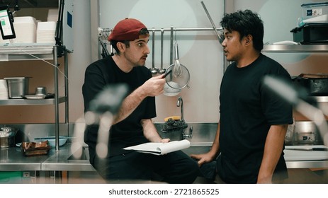 Chef manager explaining cooking workflow to employee in dark kitchen