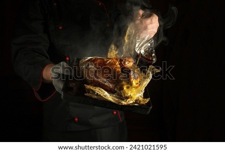 The chef manually removes the plastic bag from the chicken after baking on a baking sheet in the oven. Concept of grilling poultry in a restaurant or hotel kitchen. Dark space for recipe or menu.