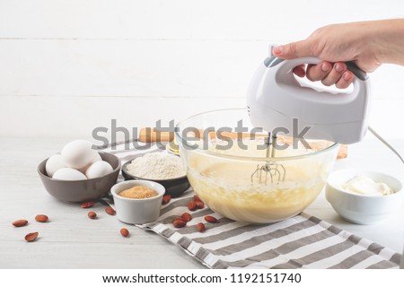 Chef with mixer in hands cooking sweet cheesecake with cooking ingredients on kitchen table white background.