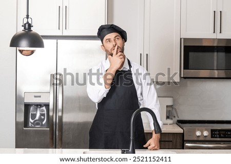 Chef on kitchen. Professional chef man in uniform on kitchen. Bearded chef, cook or baker. Male chef over kitchen background. Handsome man in chefs uniform with chefs hat cooking in the kitchen.