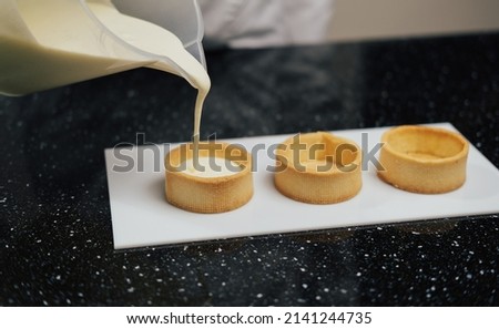 The chef pouring custard cream in the tartlets. Dessert, culinary and confectionery concept.