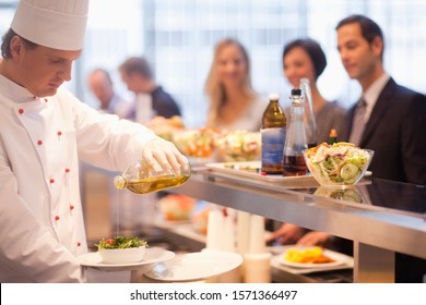 Chef pouring olive oil salad dressing on salad in work cafeteria