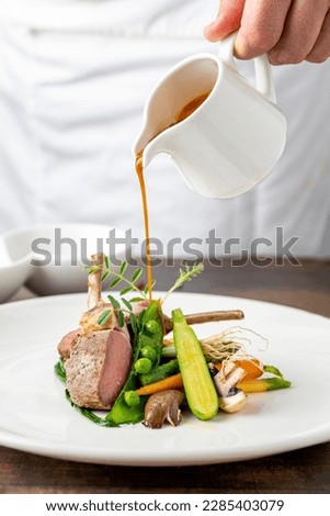 Chef pouring sauce on lamb chops with various vegetables at a fine dining restaurant