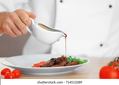 Chef Pouring Sauce On Meat Dish On Table