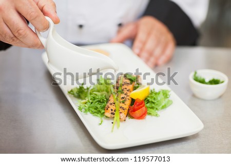 Chef pouring sauce on salmon dish in the kitchen