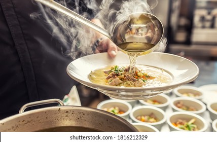 Chef pours broth into a chicken soup with noodles, meat and vegetable. - Powered by Shutterstock