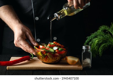 The Chef Pours Olive Oil Into A Bowl Of Salad. Cooking Tasty And Healthy Food With A Set Of Vitamins