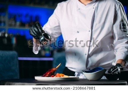 The chef pours sauce on the duck leg dish in the restaurant hall