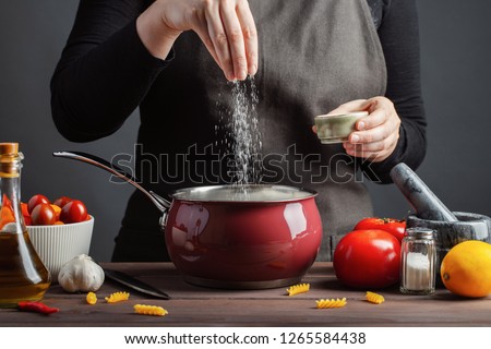 The chef preparations spaghetti and pasta, salt water, against a dark background, the concept of cooking. Woman salting water before cooking pasta fusilli