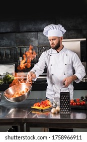 Chef Prepare Food With Fire At Kitchen Restaurant. Chef With Wok At Kitchen. Cook Male In Uniform Hold Wok With Fire At Professional Kitchen.