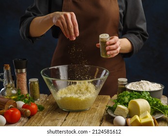 The chef prepares dishes with cheese in a professional kitchen on a wooden table on a dark background. Ingredients for cooking pizza, pasta, spaghetti, lasagna, sauce. Restaurant, hotel, cafe, banner.